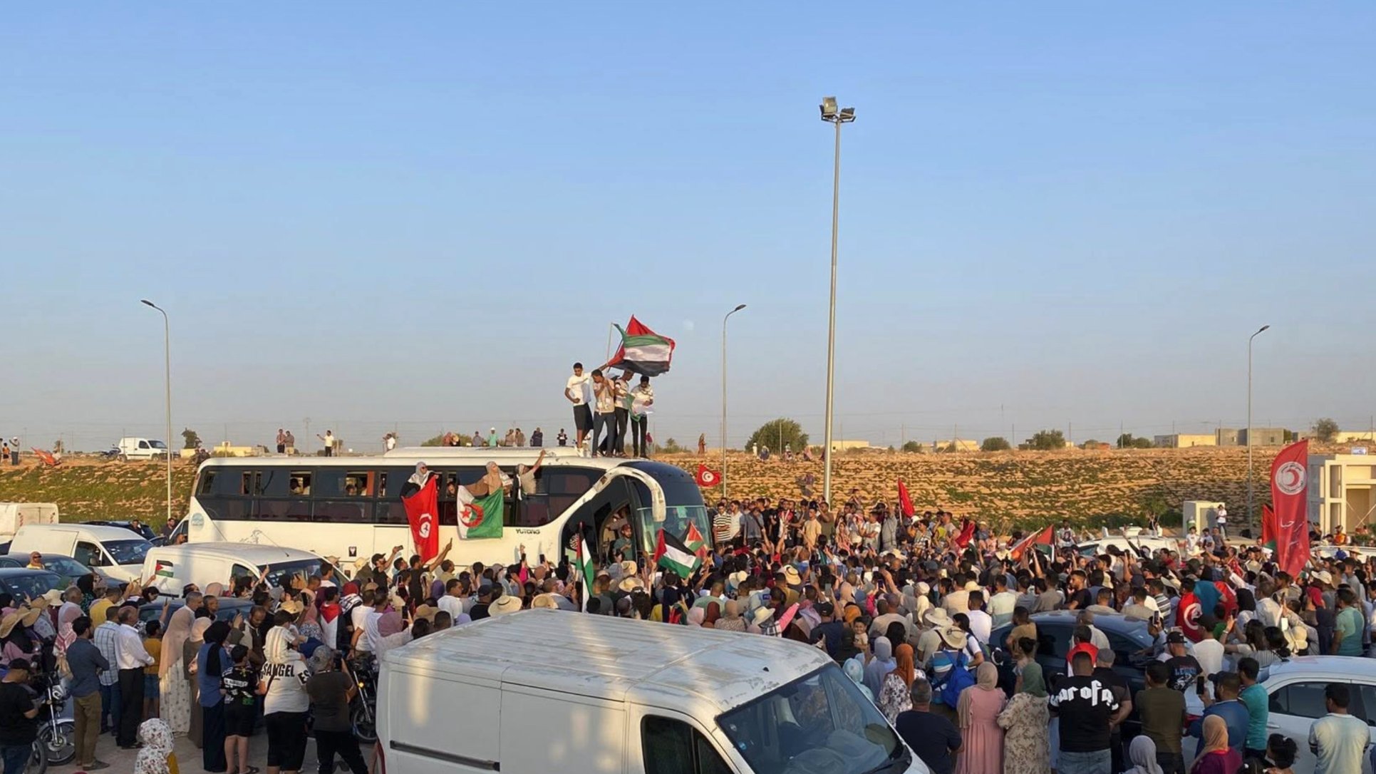 Une foule rassemblée autour d'un bus, brandissant des drapeaux et des pancartes.