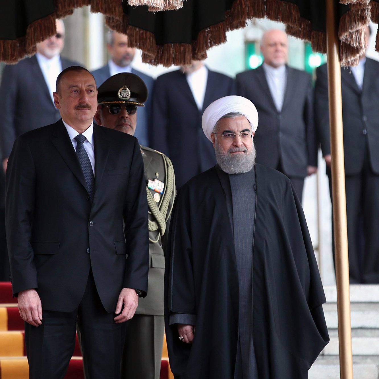 این تصویر دیداری رسمی را نشان می‌دهد که در آن دو فرد به همراه یکدیگر ایستاده‌اند. یکی از آنها در لباس رسمی و دیگری در لباس روحانی به چشم می‌خورد. در پس‌زمینه پرچم آذربایجان دیده می‌شود و تعدادی از افراد دیگر نیز در پس‌زمینه حاضرند. فضای کلی تصویری رسمی و دولتی به نظر می‌رسد.