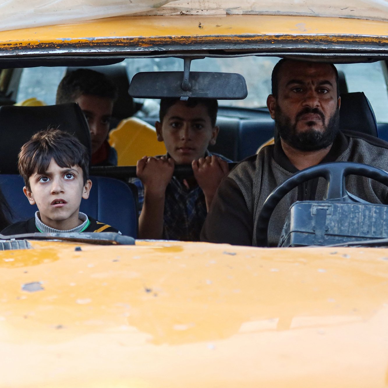 Un homme conduit une vieille voiture avec des enfants inquiets à l'intérieur.