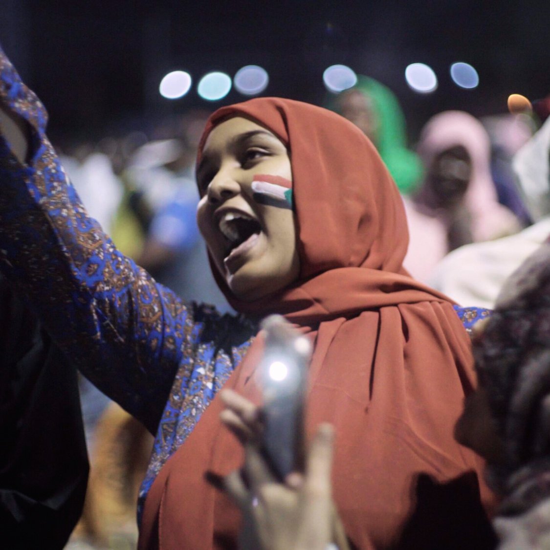 Groupe de jeunes célébrant avec enthousiasme, drapeaux et sourires.