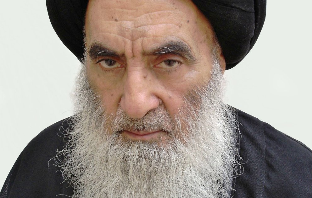 الصورة تُظهر رجلًا مسنًّا ذو لحية بيضاء وشعر داكن تحت عمامة سوداء. يبدو عليه الوقار والجدية. يرتدي ثوبًا داكنًا، مما يعكس نمطًا تقليديًا في اللباس. الخلفية بسيطة ووردية اللون، مما يبرز ملامح وجهه.