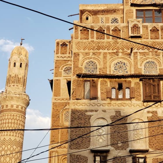 Vieilles maisons en briques, motifs géométriques, minaret élancé sous un ciel bleu.