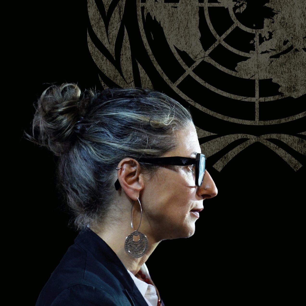 Donna con occhiali e capelli raccolti, in un ambiente con il logo delle Nazioni Unite sullo sfondo.