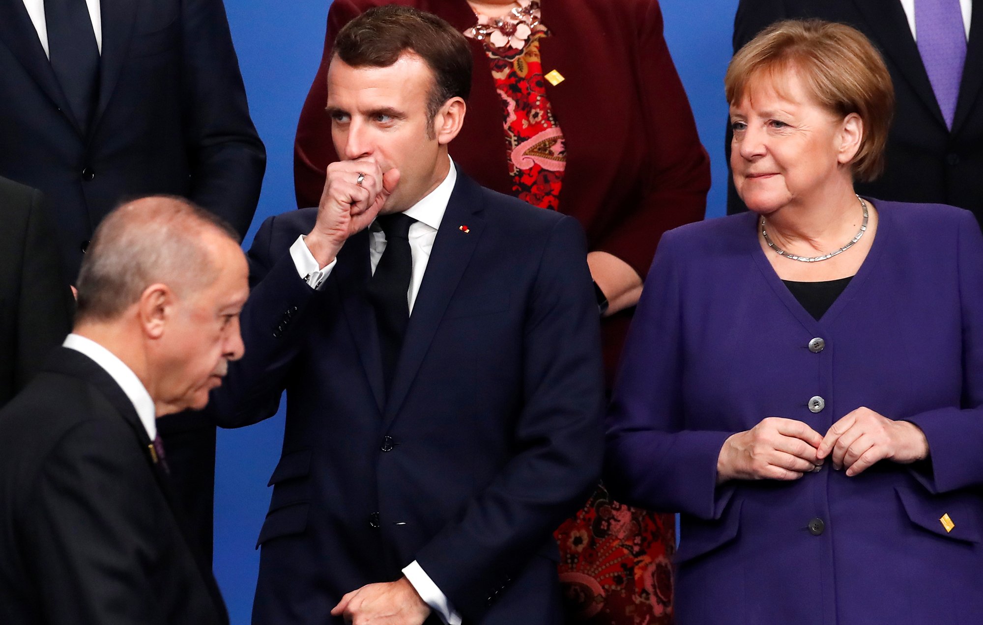 L'image montre un groupe de dirigeants politiques rassemblés lors d'un événement officiel. Au premier plan, on peut voir un homme qui se tient à gauche, probablement en train de parler ou d'écouter. Au centre, un homme en costume sombre semble réfléchir, avec une main devant sa bouche. À droite, une femme porte un vêtement violet et observe la scène avec un léger sourire. L'atmosphère semble être formelle, typique des rencontres diplomatiques.