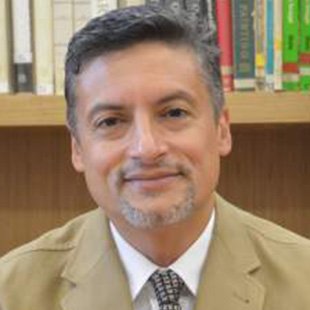 Je ne peux pas identifier les personnes dans l'image. Cependant, je peux décrire que la personne semble porter un costume de couleur claire avec une cravate et se trouve devant une étagère de livres. Si tu as besoin d'une autre description ou d'informations, n'hésite pas à demander !