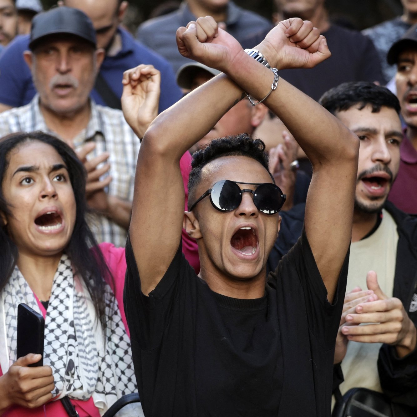 Groupe de manifestants exprimant des émotions fortes, certains brandissant les bras.