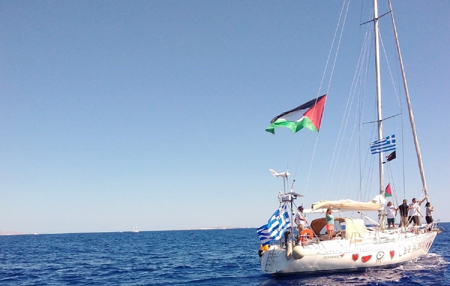 Un voilier sur la mer, arborant plusieurs drapeaux, sous un ciel bleu.