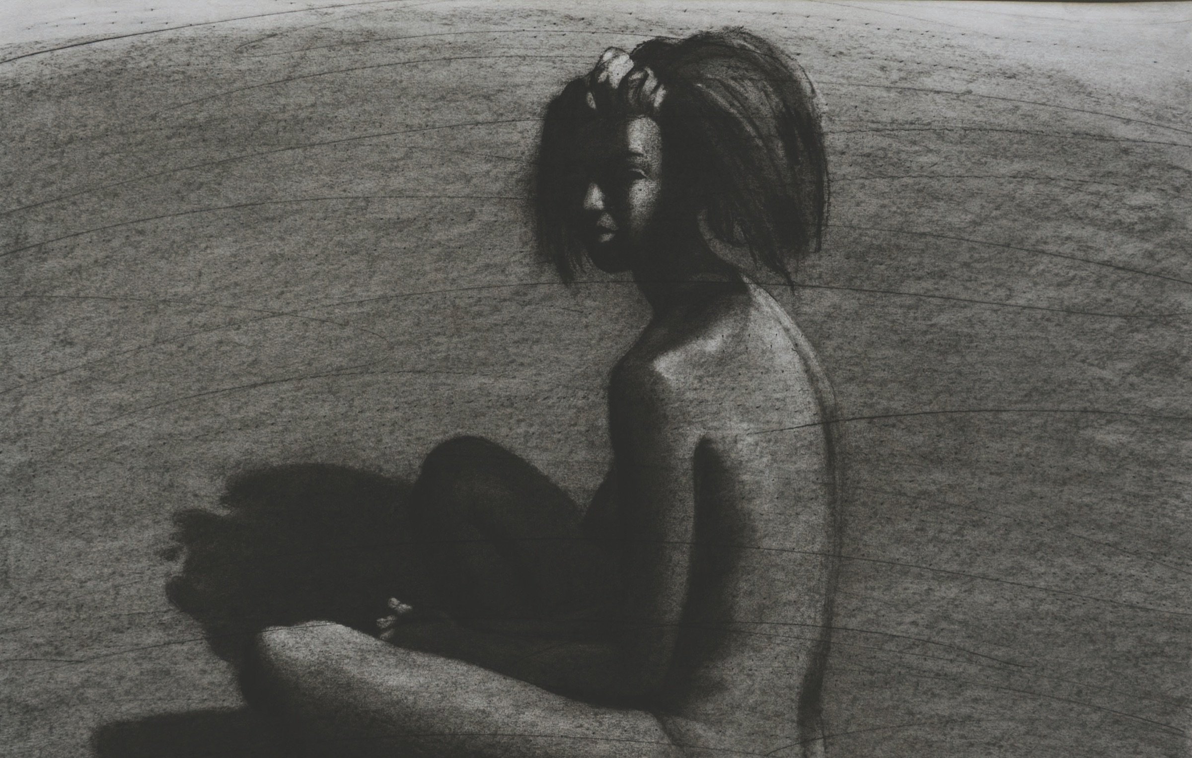 The image depicts a nude figure seated with their back to the viewer, captured in a monochromatic charcoal style. The figure has a slightly turned profile, showcasing a sense of contemplation. The body is rendered with soft, flowing lines, contrasting against the darker, shadowy background. The light appears to create a dramatic play of shadows, emphasizing the contours and curves of the figure. The overall mood is introspective and artistic, focusing on the human form and its relationship with light and darkness.