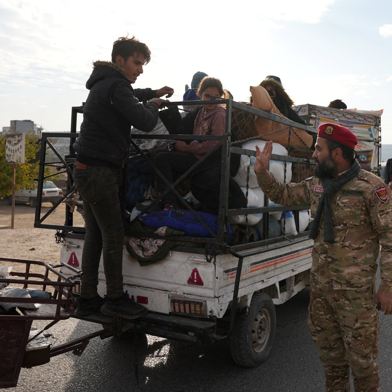 Des personnes sur une camionnette, un soldat gesticule au sol. Atmosphère tendue.