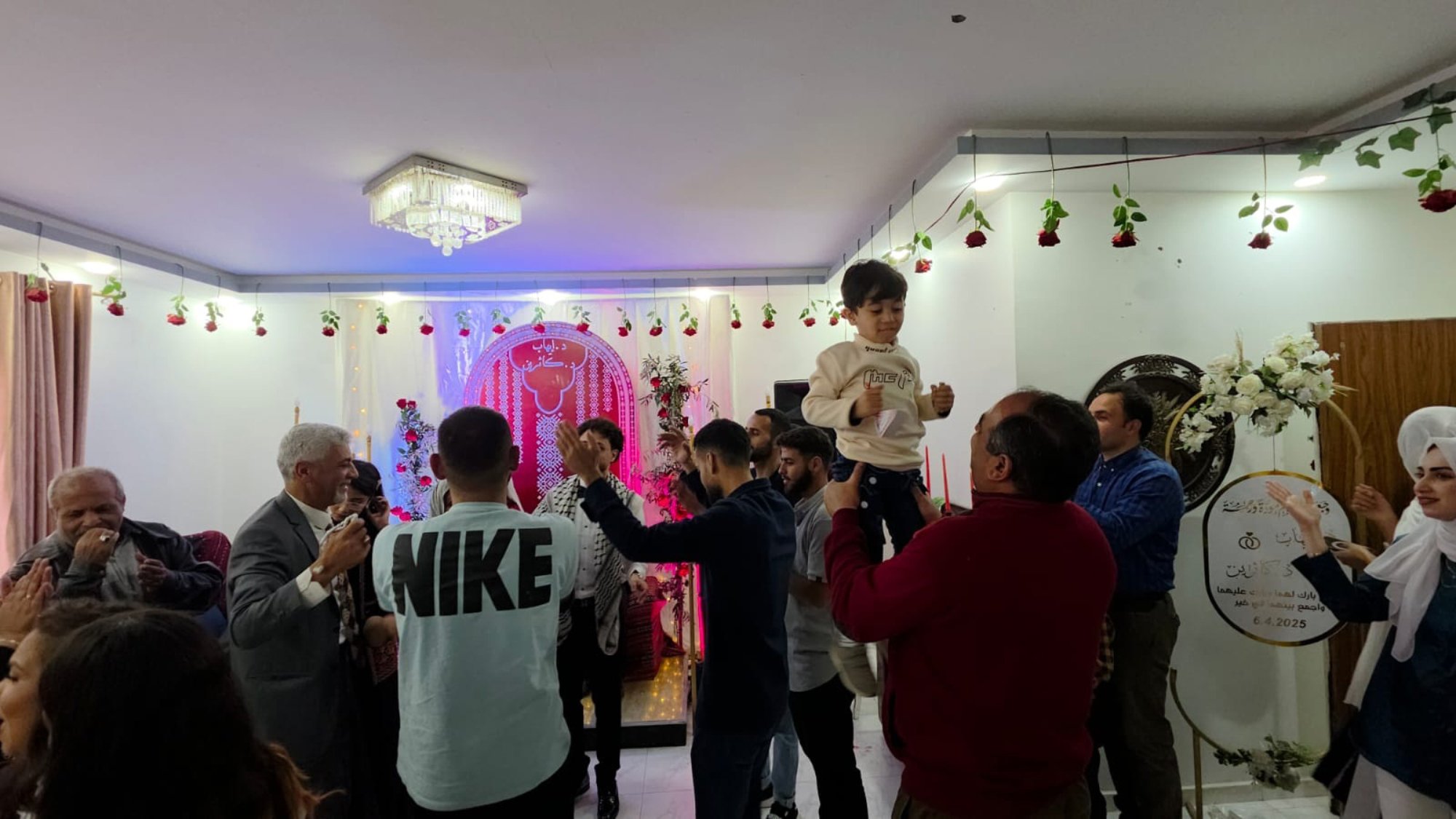 Una festa con persone che ballano, decorazioni floreali e un bambino in braccio.