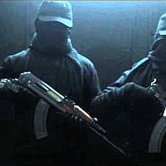 L'image montre deux individus habillés en noir, portant des masques et des casquettes. Ils tiennent des armes à feu, et l'un d'eux tient aussi un document. L'arrière-plan est sombre, ce qui accentue l'atmosphère mystérieuse de la scène.