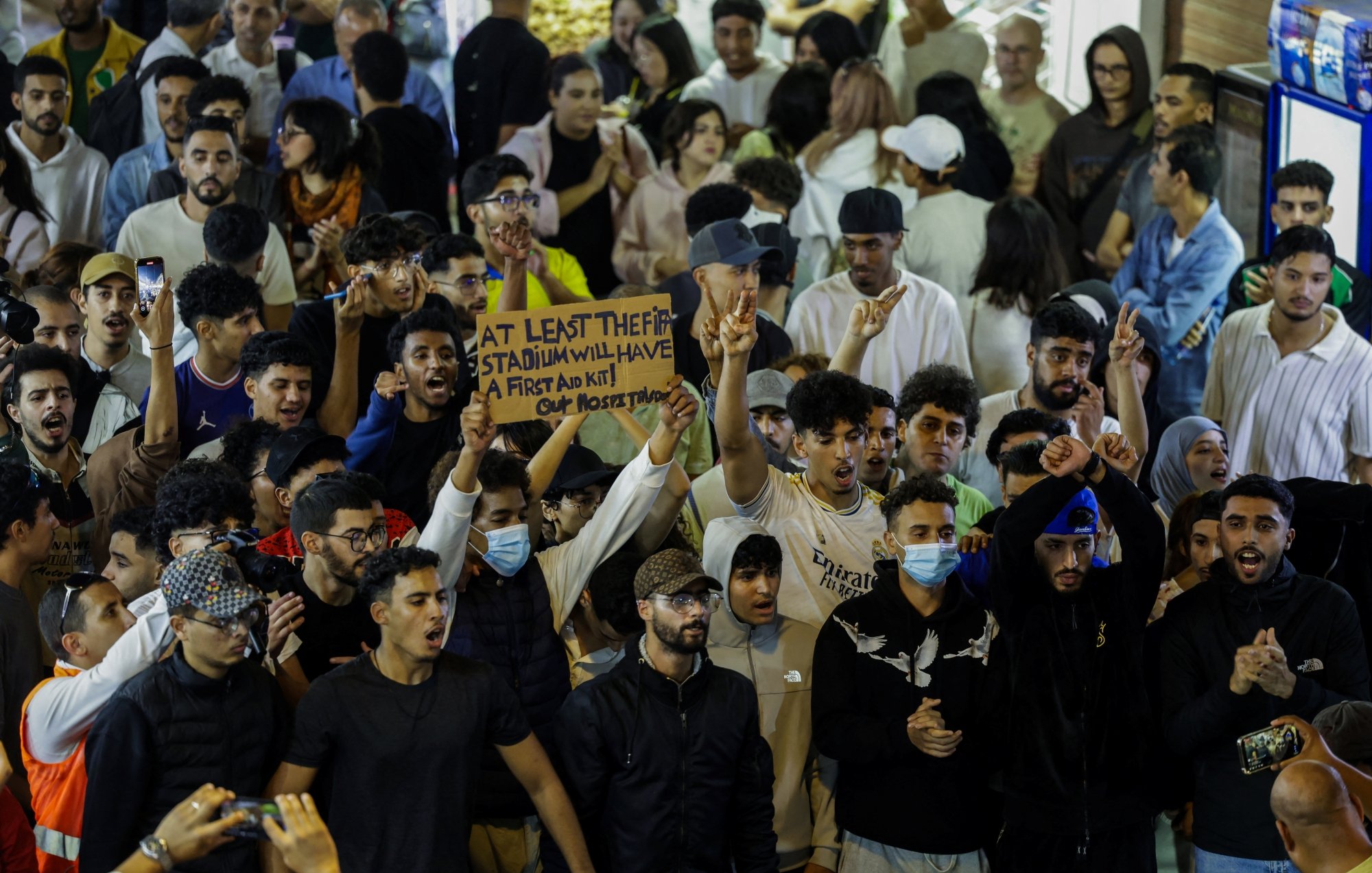 حشود من الناس في مكان مزدحم، يرفعون لافتة ويهتفون، مع تباين في الألوان والملابس.