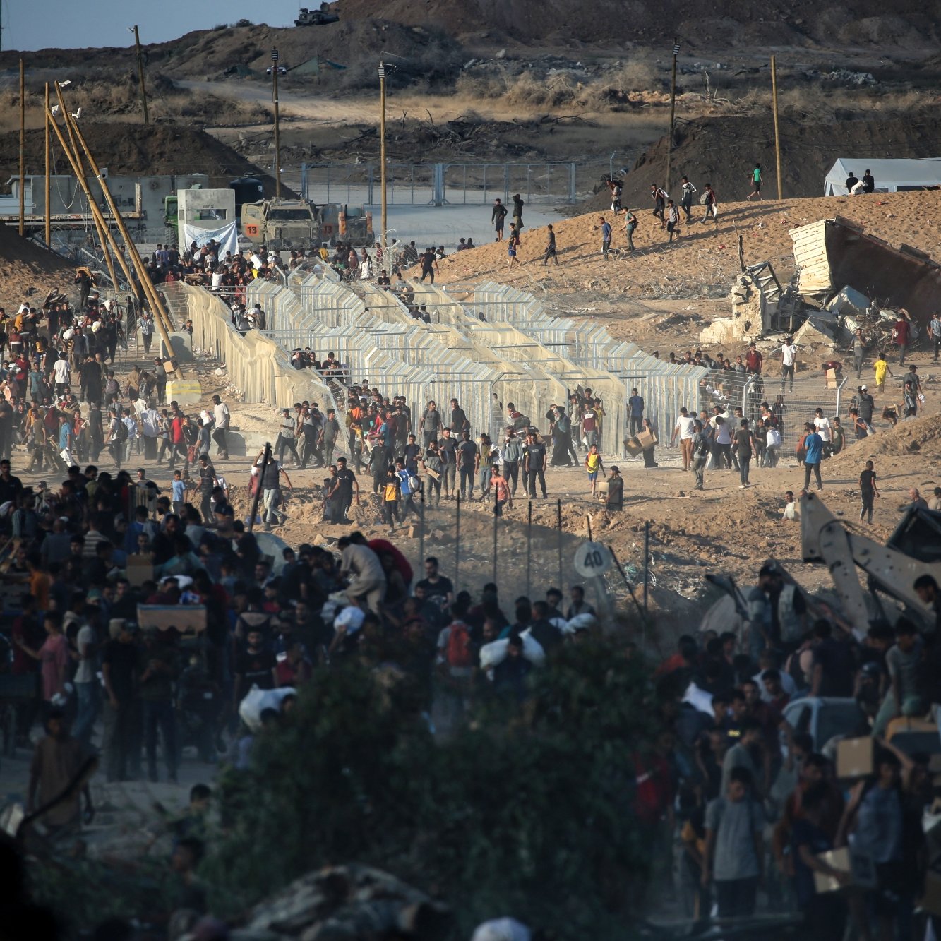 Une foule se rassemble près de clôtures dans un paysage aride et dévasté.