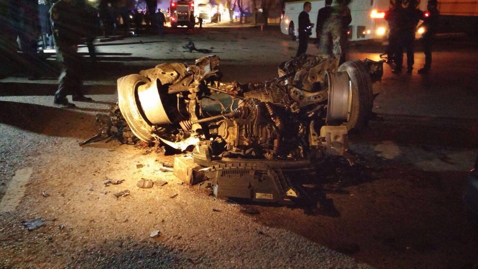 تصویر نشاندهنده یک تصادف خودرو است که در آن یک خودرو به طور کامل واژگون شده و روی سقف خود قرار دارد. قطعات خودرو به اطراف پخش شده و آسیبهای قابل توجهی به آن وارد شده است. صحنه روشنایی کمی دارد و ممکن است در یک شب یا در شرایط کم نور باشد. همچنین، افرادی در پسزمینه دیده میشوند که احتمالاً در حال رسیدگی به وضعیت هستند.