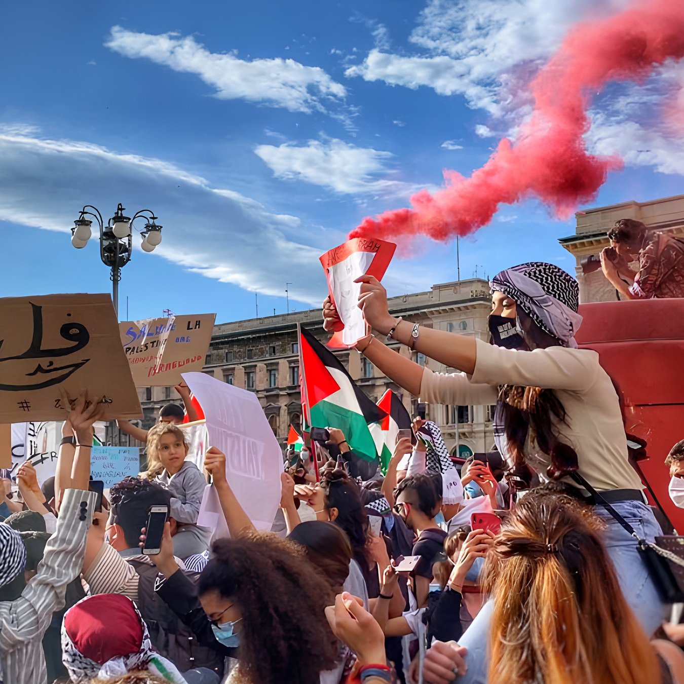 Una manifestazione colorata con fumogeni rossi e cartelli per la Palestina.