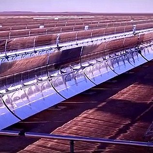 L'image montre un paysage d'énergie solaire, probablement un champ de miroirs ou de panneaux solaires. On peut voir plusieurs lignes de miroirs courbés, orientés vers le soleil. Ces miroirs concentrent les rayons solaires pour produire de l'énergie. L'arrière-plan est désertique ou plat, suggérant que l'installation est située dans une région ensoleillée. L'ambiance générale évoque une technologie moderne et des initiatives en faveur des énergies renouvelables.