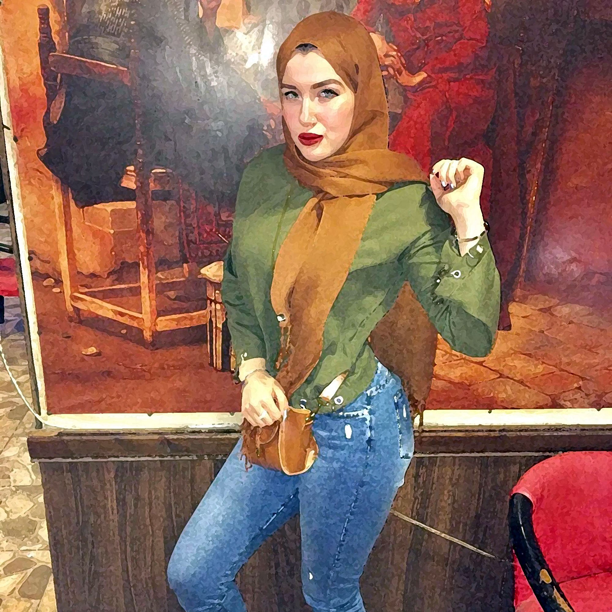 L'immagine mostra una giovane donna che indossa un hijab color marrone e una camicia verde. È in piedi con una mano sulla vita e l'altra sollevata, con un'espressione sicura. Indossa jeans attillati e scarpe marroni. Sullo sfondo si intravede un dipinto o una decorazione murale che aggiunge un tocco di colore all'ambiente. L'illuminazione sembra calda, contribuendo a un'atmosfera accogliente.