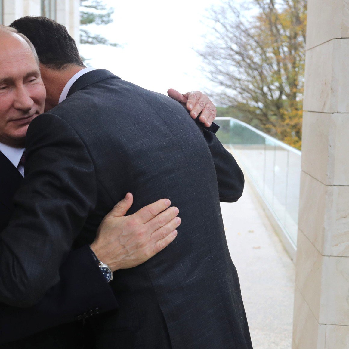 در این تصویر، دو مرد در حالیکه به یکدیگر نزدیک شده‌اند، در حال بغل کردن هم هستند. یکی از آنها با لباسی رسمی و کراوات به نظر می‌رسد و دیگری نیز ظاهری مشابه دارد. پس‌زمینه تصویر شامل دیواری سنگی و فضایی سبز است. حالت کلی تصویر نشان‌دهنده نزدیکی یا همدلی بین این دو نفر است.