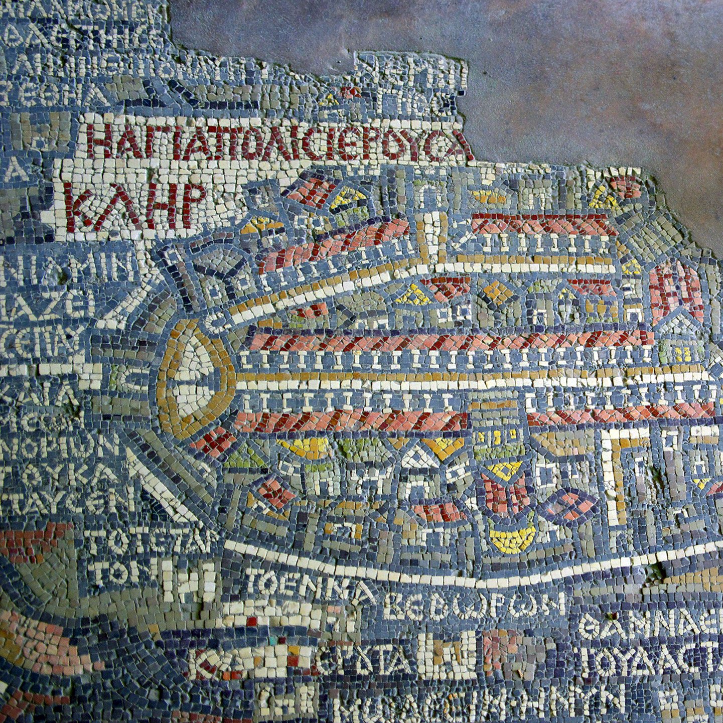 این تصویر نمایی از یک موزاییک قدیمی را نشان می‌دهد که نقشه‌ای از یک شهر تاریخی را به تصویر می‌کشد. در این موزاییک، جزئیات مختلفی از ساختمان‌ها، خیابان‌ها و نمادهای شهری مشاهده می‌شود. خطوط و اشکال با قطعات کوچک کاشی‌های رنگی طراحی شده‌اند و نوشته‌هایی به زبان یونانی در اطراف آن دیده می‌شود. این اثر هنری می‌تواند به عنوان یک سند تاریخی از زندگی شهری و معماری در دوران گذشته تعبیر شود.