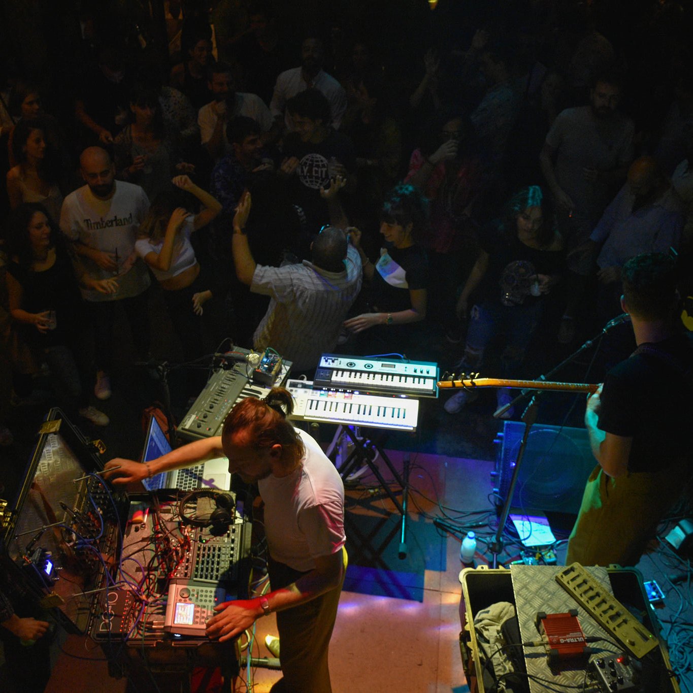 Concert animé avec des musiciens, des synthétiseurs et une foule dans une ambiance festive.