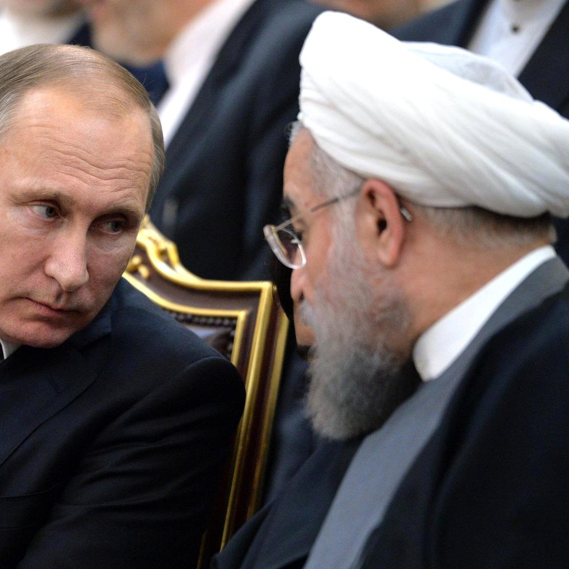 تظهر الصورة اثنين من الشخصيات السياسية يجلسان جنبًا إلى جنب في مناسبة رسمية. الشخص الأول يرتدي بدلة داكنة مع ربطة عنق باللون الوردي ويبدو جادًا وهو ينظر إلى الشخص الآخر. الشخص الثاني يرتدي ملابس تقليدية إسلامية تشمل عمامة، ويتحدث مع الشخص الأول. الخلفية تحتوي على أشخاص آخرين وجو عام رسمي.