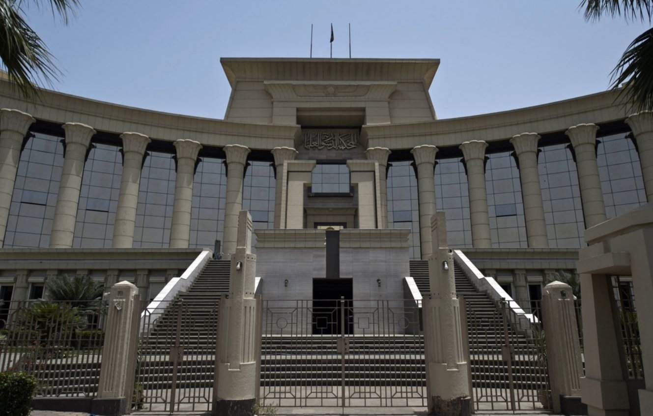 L'image montre un bâtiment imposant, probablement une institution judiciaire, avec une architecture moderne. La façade est ornée de colonnes majestueuses et de grandes fenêtres réfléchissantes, créant une impression de grandeur. Il y a des escaliers menant à l'entrée principale, qui semble être encadrée par des éléments décoratifs. Le ciel est dégagé, suggérant une journée ensoleillée. Des palmiers sont visibles sur les côtés, ajoutant une touche tropicale à l'environnement.