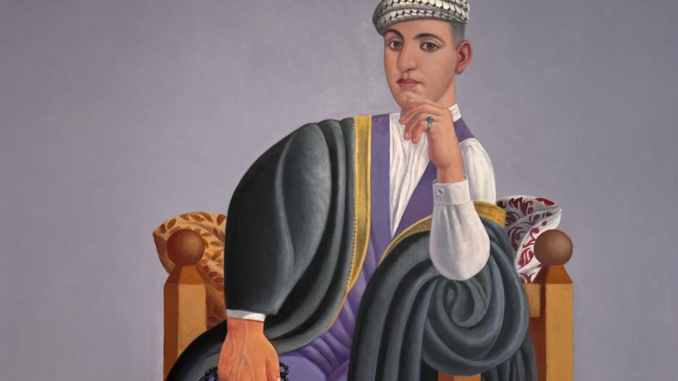 Un homme assis, vêtu traditionnellement, sur une chaise, avec un tapis coloré en dessous.