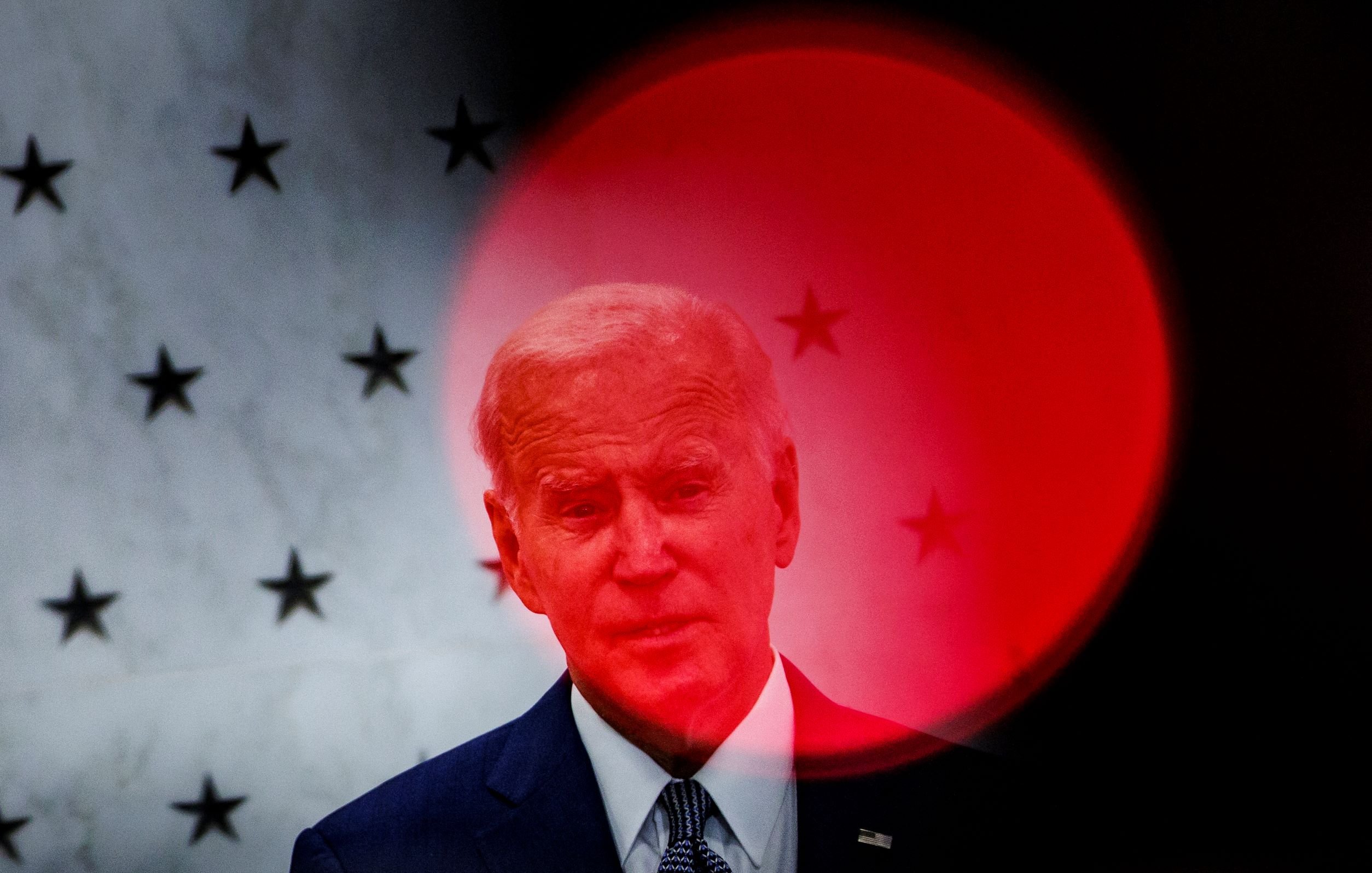 تظهر الصورة شخصاً يقف أمام خلفية بها نجوم، مع تأثير بصري يشير إلى دائرة حمراء غير واضحة. يبدو أن الشخص يتحدث أو يدلي ببيان، حيث يُركَّز الضوء عليه بشكل يجعله بارزاً. الخلفية والظلال تضفي طابعاً درامياً على الصورة.