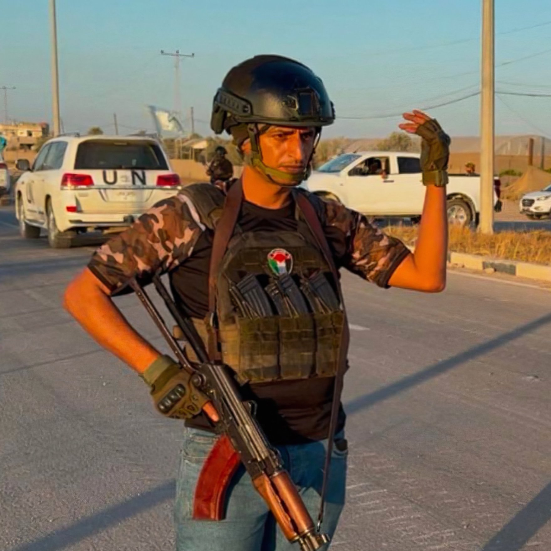 Un homme armé, en tenue militaire, se tient sur une route avec des voitures en arrière-plan.