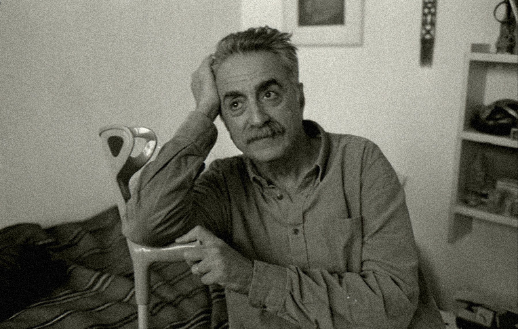 Homme pensif, assis, avec une canne, dans une pièce simple et lumineuse.