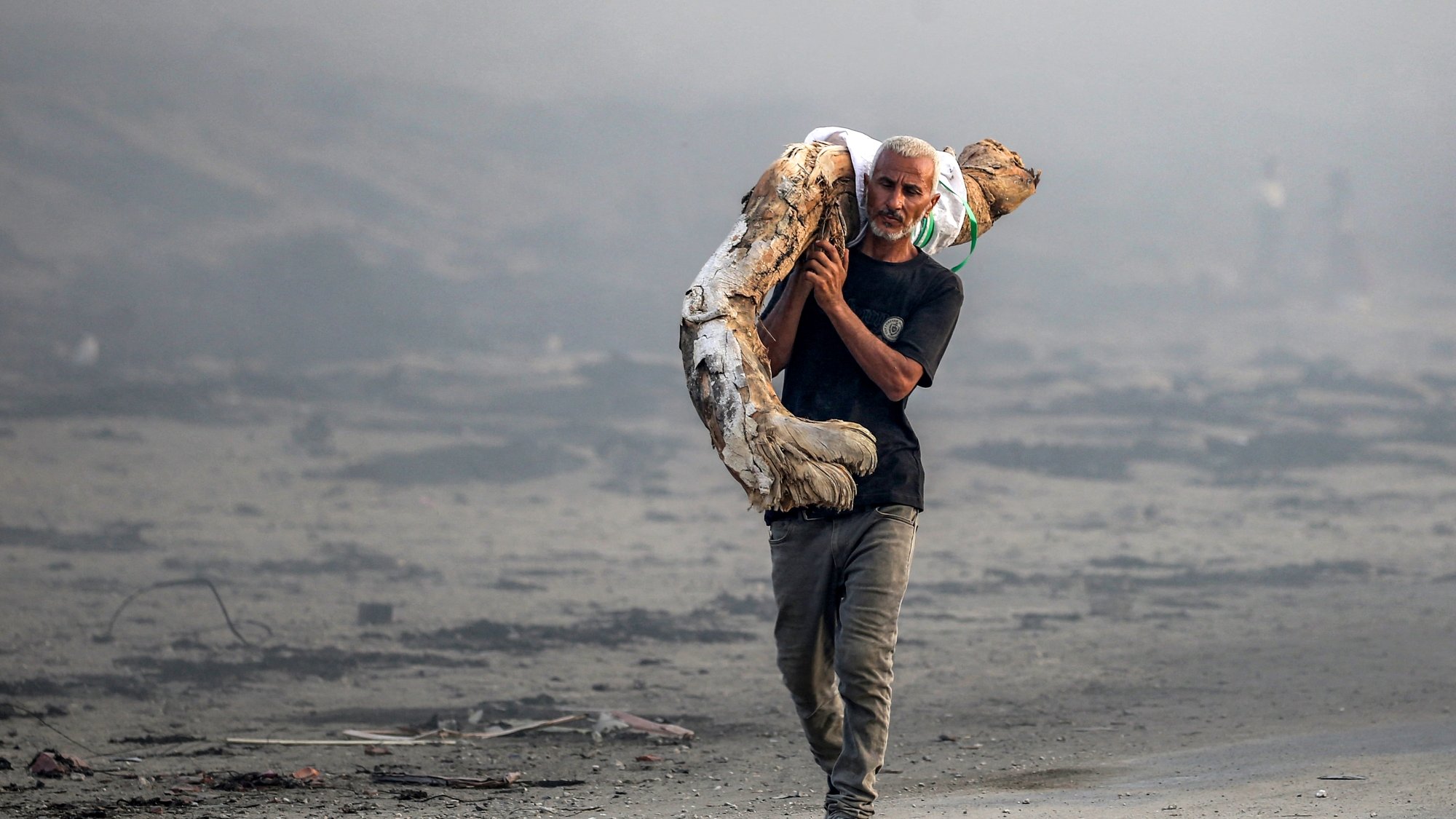 Un uomo attraversa un paesaggio desolato, portando un oggetto pesante sulle spalle.
