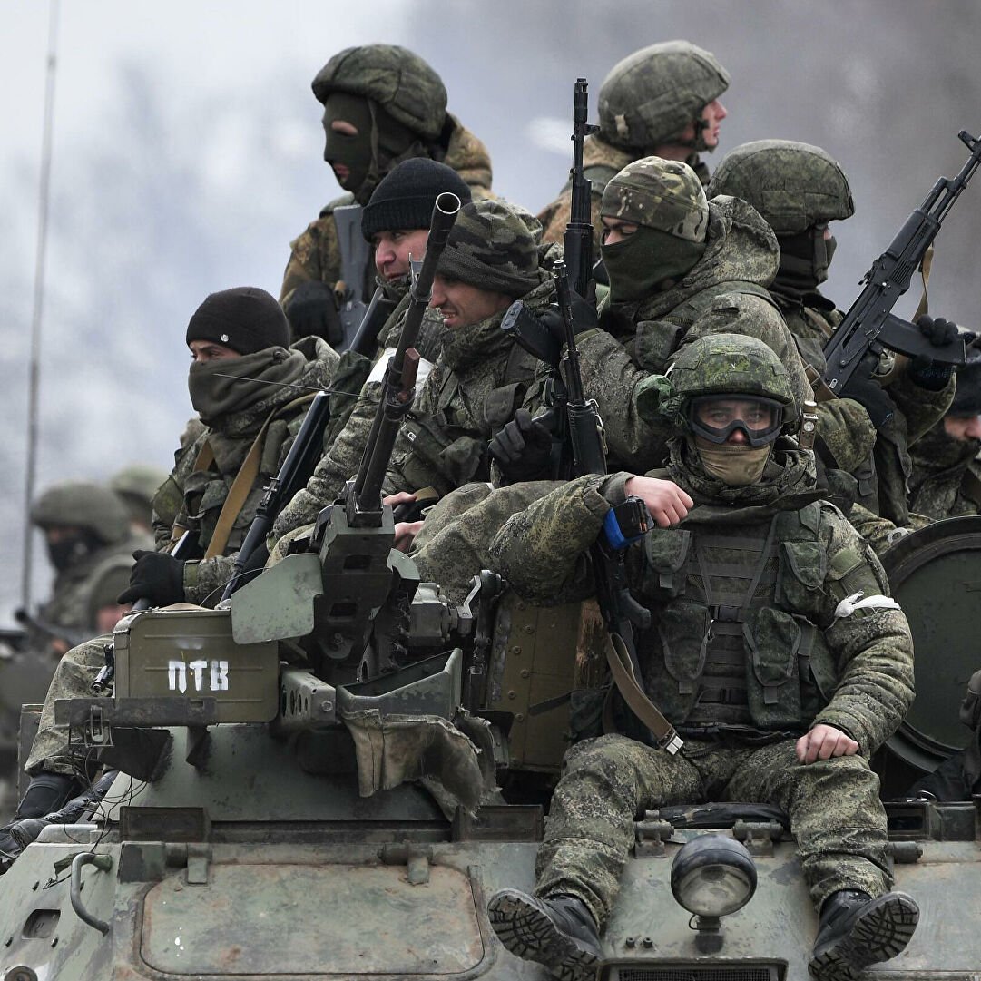 L'image montre un groupe de soldats armés, équipés de vêtements militaires et de casques, se tenant sur un véhicule blindé. Ils semblent en position attentive, probablement lors d'une opération militaire. L'ambiance est sérieuse et le paysage environnant est sombre, ce qui renforce le contexte militaire et opérationnel. Les soldats portent des masques et des lunettes, ce qui indique qu'ils sont préparés pour des conditions difficiles.