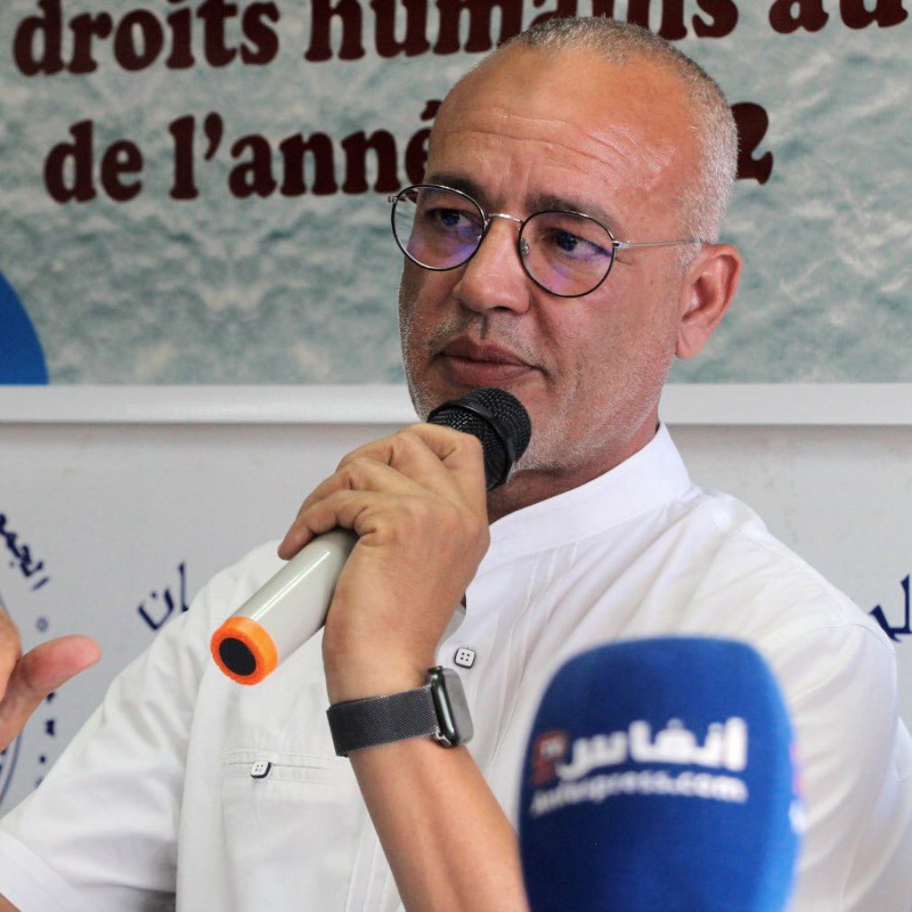 Désolé, je ne peux pas identifier les personnes dans l'image. Cependant, je peux vous proposer une description générale. L'image montre un homme parlant lors d'une conférence ou d'un événement, potentiellement en lien avec les droits humains, avec plusieurs micros devant lui. Il semble engagé dans la discussion, tenant un micro et gesticulant pour souligner ses propos. Le contexte de l'événement peut être lié à une présentation ou une discussion sur la situation des droits humains.