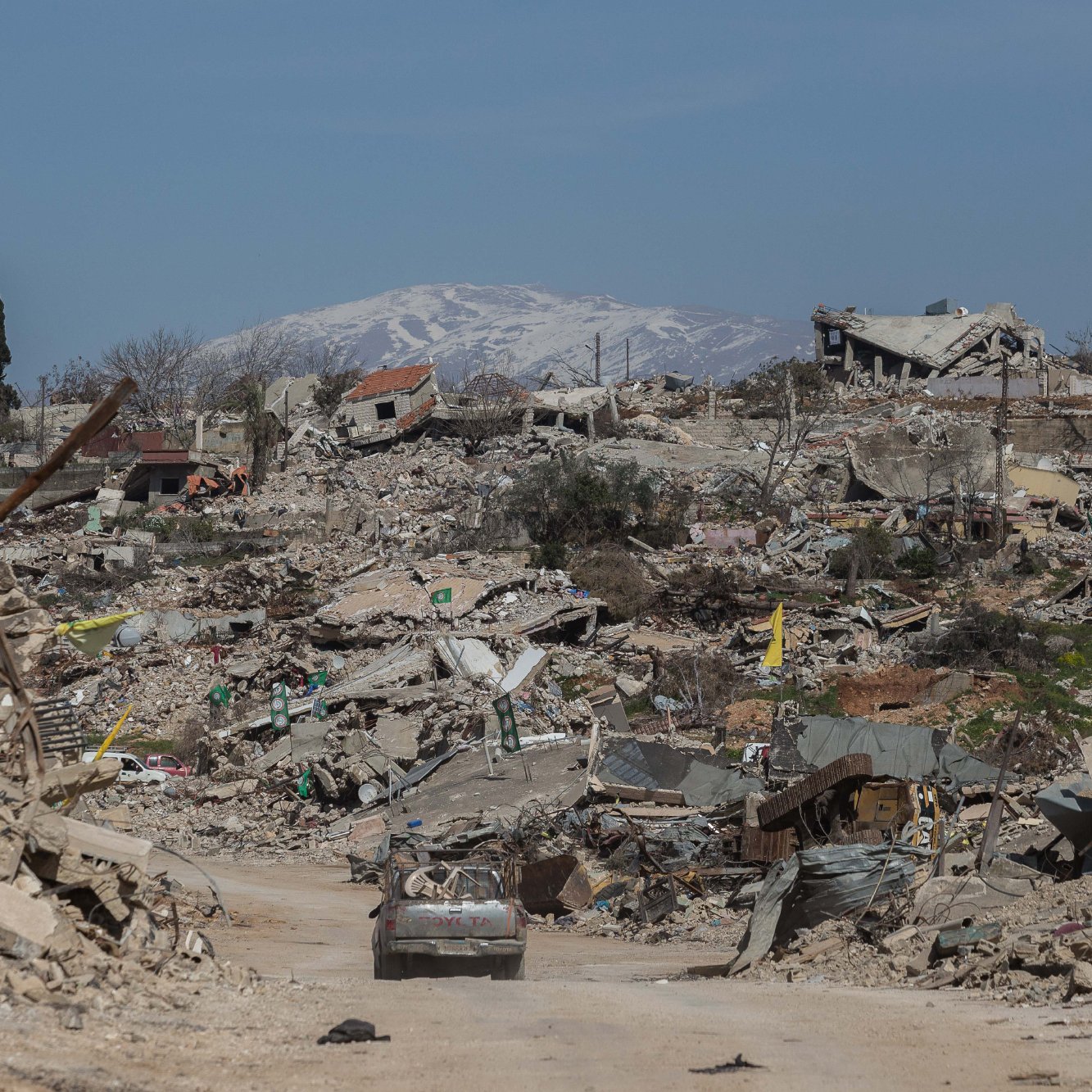 Un paysage dévasté avec des bâtiments en ruines et des montagnes enneigées au loin.