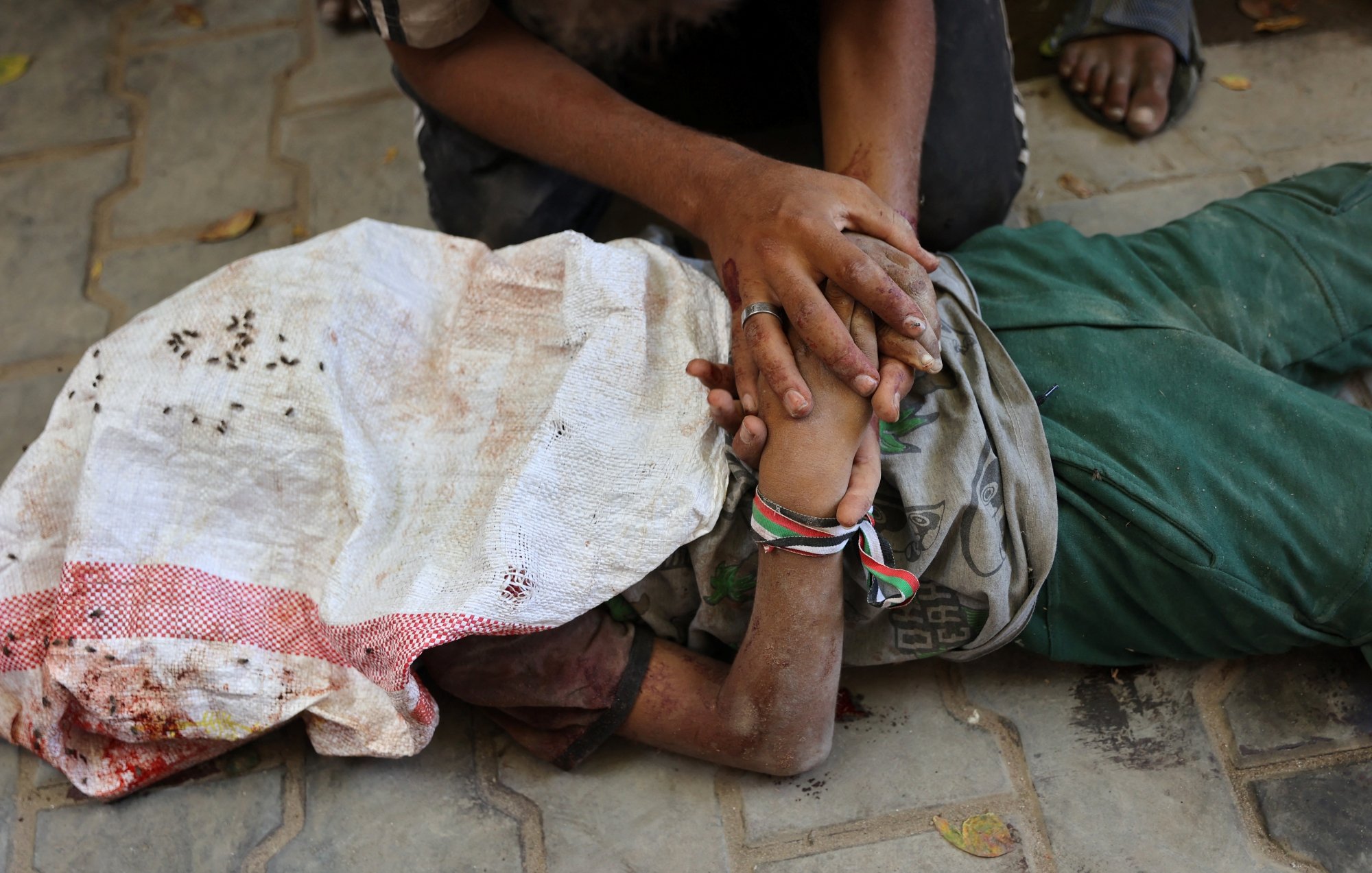 A person lying on the ground, covered in a cloth, with another person holding their hand.