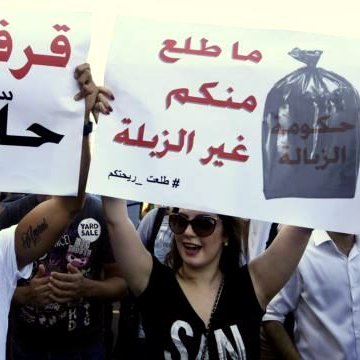 L'image montre une manifestation où des personnes tiennent des pancartes. Les messages sur les pancartes évoquent des revendications concernant la situation dans leur pays. L'une des pancartes semble exprimer un mécontentement face à la gestion des déchets, tandis que l'autre parle d'un désir de changement ou d'amélioration. Les manifestants semblent passionnés et engagés dans leur lutte. L'ambiance générale suggère une mobilisation citoyenne.