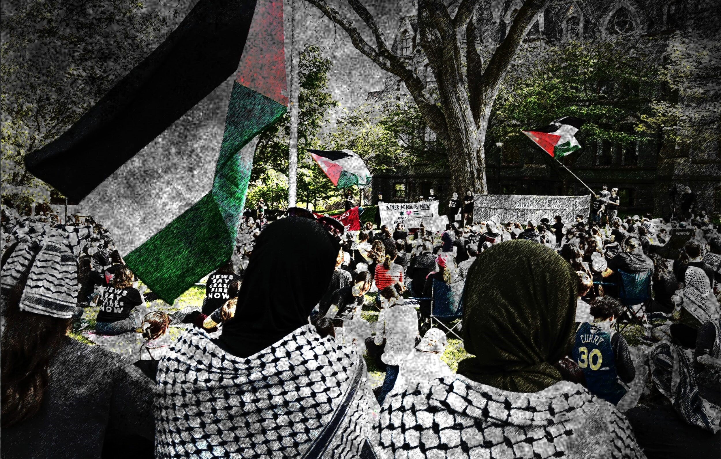 L'immagine mostra una manifestazione in cui partecipano molte persone, alcune delle quali indossano sciarpe tradizionali palestinesi. Si possono vedere delle bandiere palestinesi sventolare sullo sfondo. La scena è caratterizzata da una grande affluenza di partecipanti, con un'atmosfera di attivismo e solidarietà. Gli alberi e l'architettura circostante forniscono un contesto urbano alla manifestazione, suggerendo un forte impegno per una causa sociale.