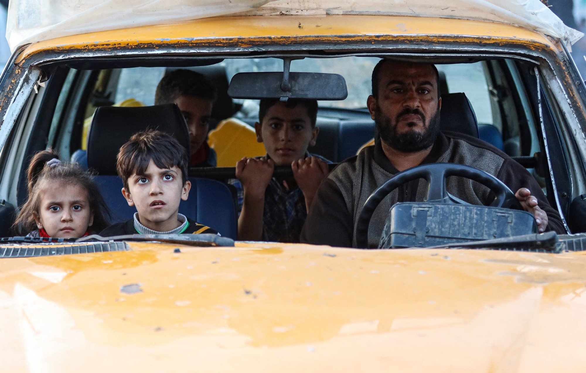 Un uomo alla guida di un'auto con bambini nel sedile anteriore, sguardi preoccupati.