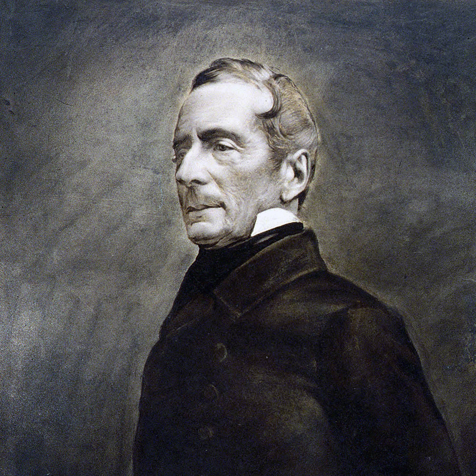 L'image montre un portrait en noir et blanc d'un homme d'âge moyen, vêtu d'un manteau sombre. Son expression est sérieuse et réfléchie, avec des traits du visage bien définis. Il a les cheveux légèrement ondulés, peignés vers l'arrière, et il porte un col montant. L'arrière-plan est flou, mettant en valeur le sujet du portrait. L'ensemble a un aspect classique et intemporel, caractéristique des portraits du 19ème siècle.