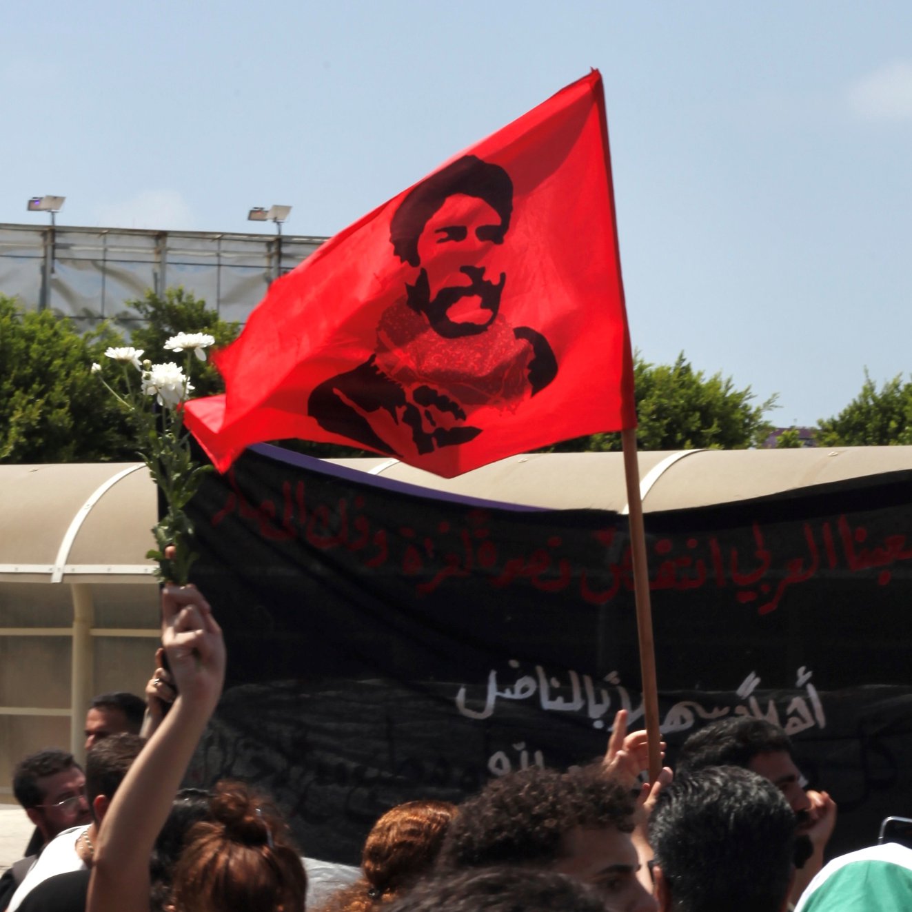 Une foule brandit un drapeau rouge avec un portrait en noir et blanc.