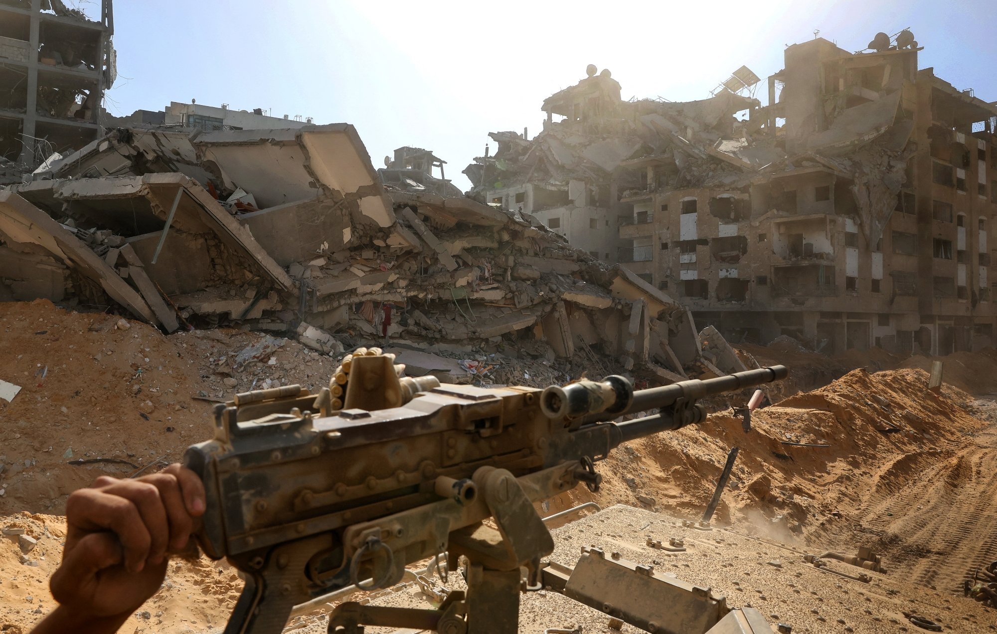 Una zona devastata, edifici crollati e un fucile appoggiato su un treppiede.