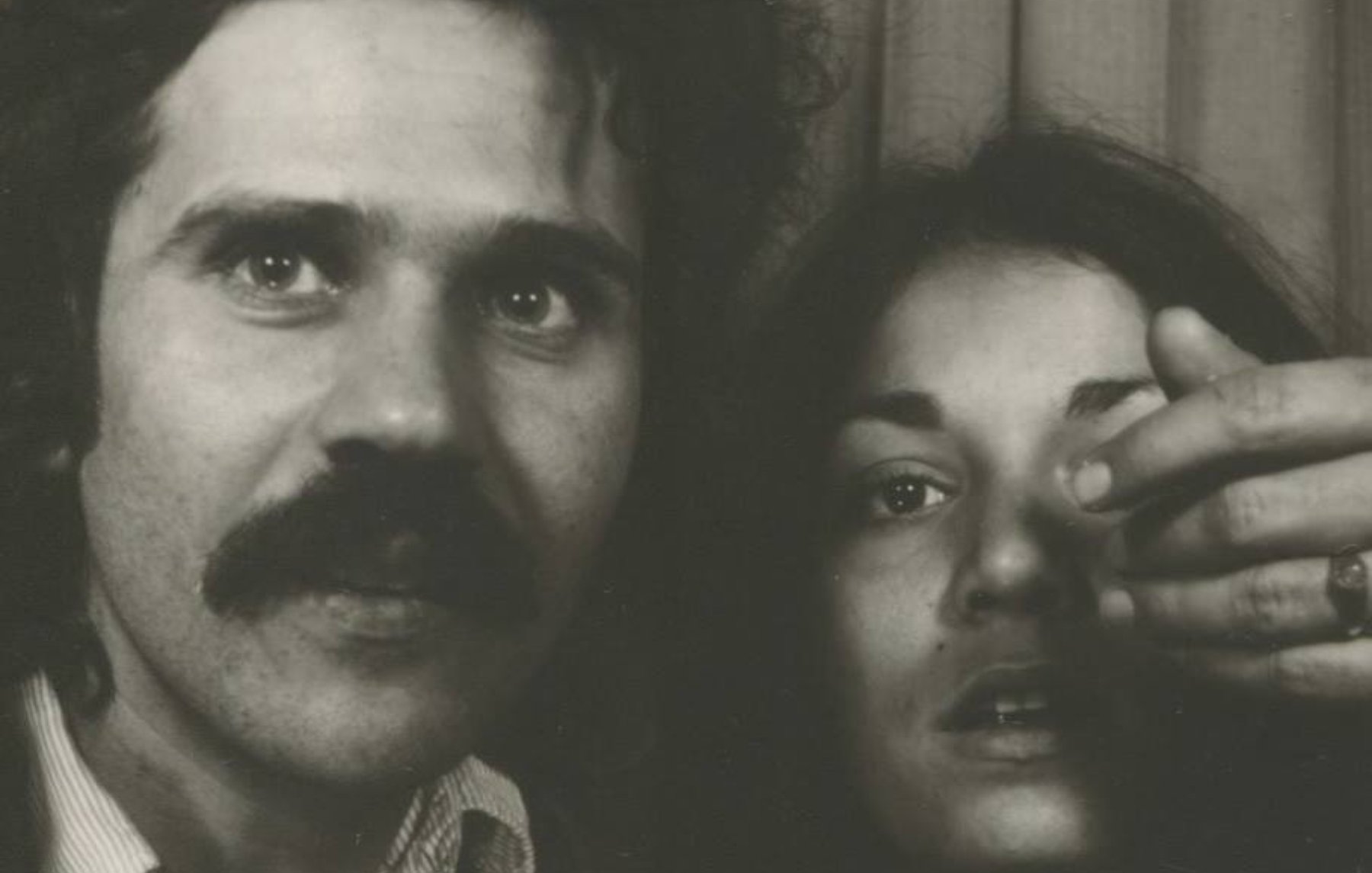 Un homme avec une moustache et une femme montrant un doigt vers l'objectif.