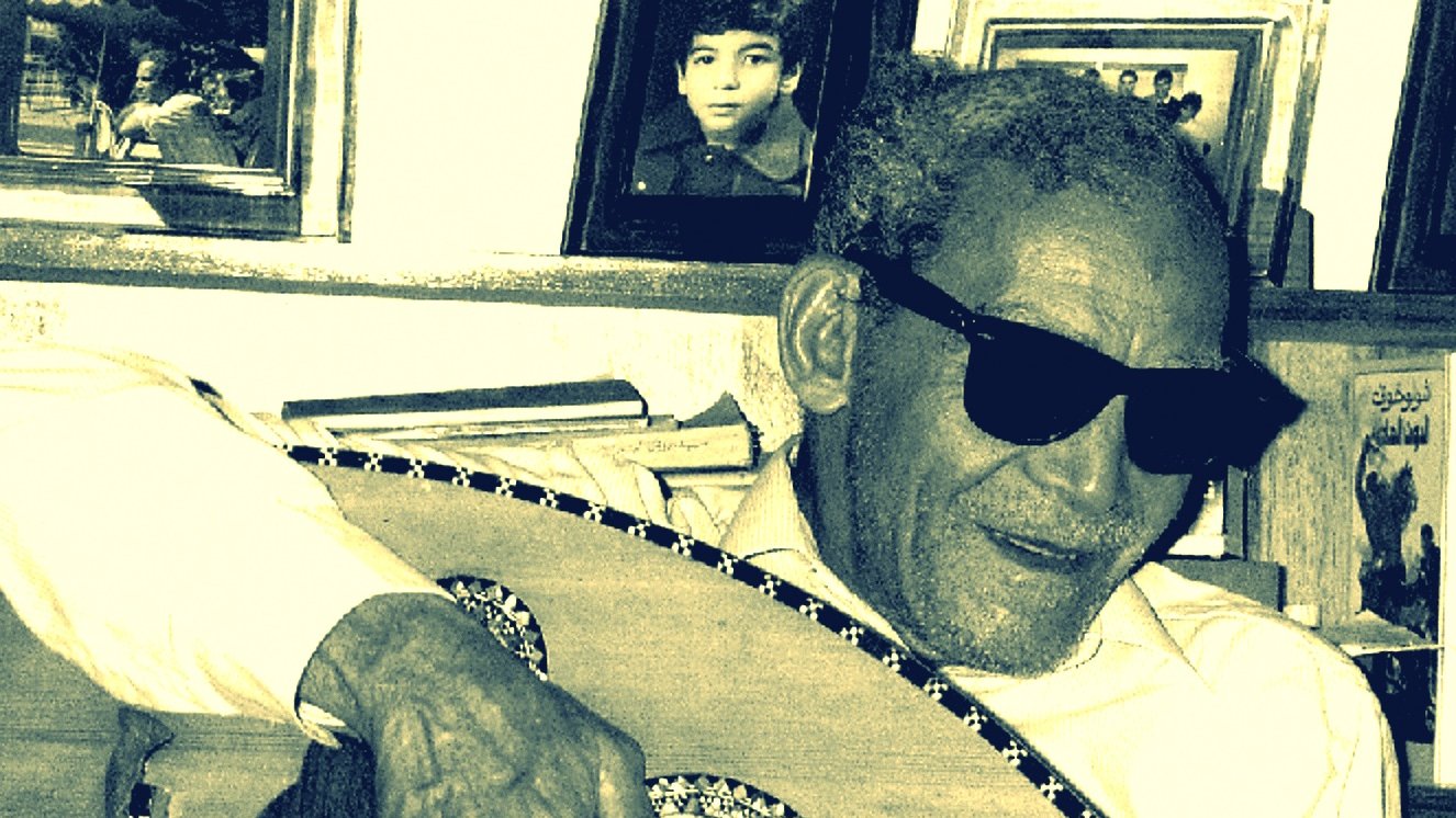 الصورة تظهر رجلًا مسنًا يرتدي نظارات شمسية ويعزف على آلة العود. يبدو سعيدًا ومسترخيًا، محاطًا بإطارات صور على الجدار خلفه. الأسلوب الذي يقدّم به العزف يعكس شغفه بالموسيقى. الأجواء تدل على لمسة من الح nostalgia، مع تفاصيل تعكس العناية والحنين إلى الماضي.