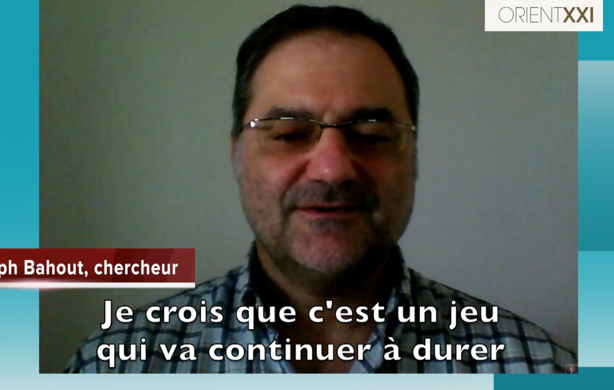L'image montre un homme apparaissant en vidéoconférence. Il porte des lunettes et un chemisier à carreaux. Le texte en bas de l'image indique son nom, "Joseph Bahout, chercheur", suivi d'une citation où il exprime son opinion sur une situation, affirmant qu'il croit que "c'est un jeu qui va continuer à durer". Le fond est simple, et l'interface semble être d'une plateforme de communication vidéo.