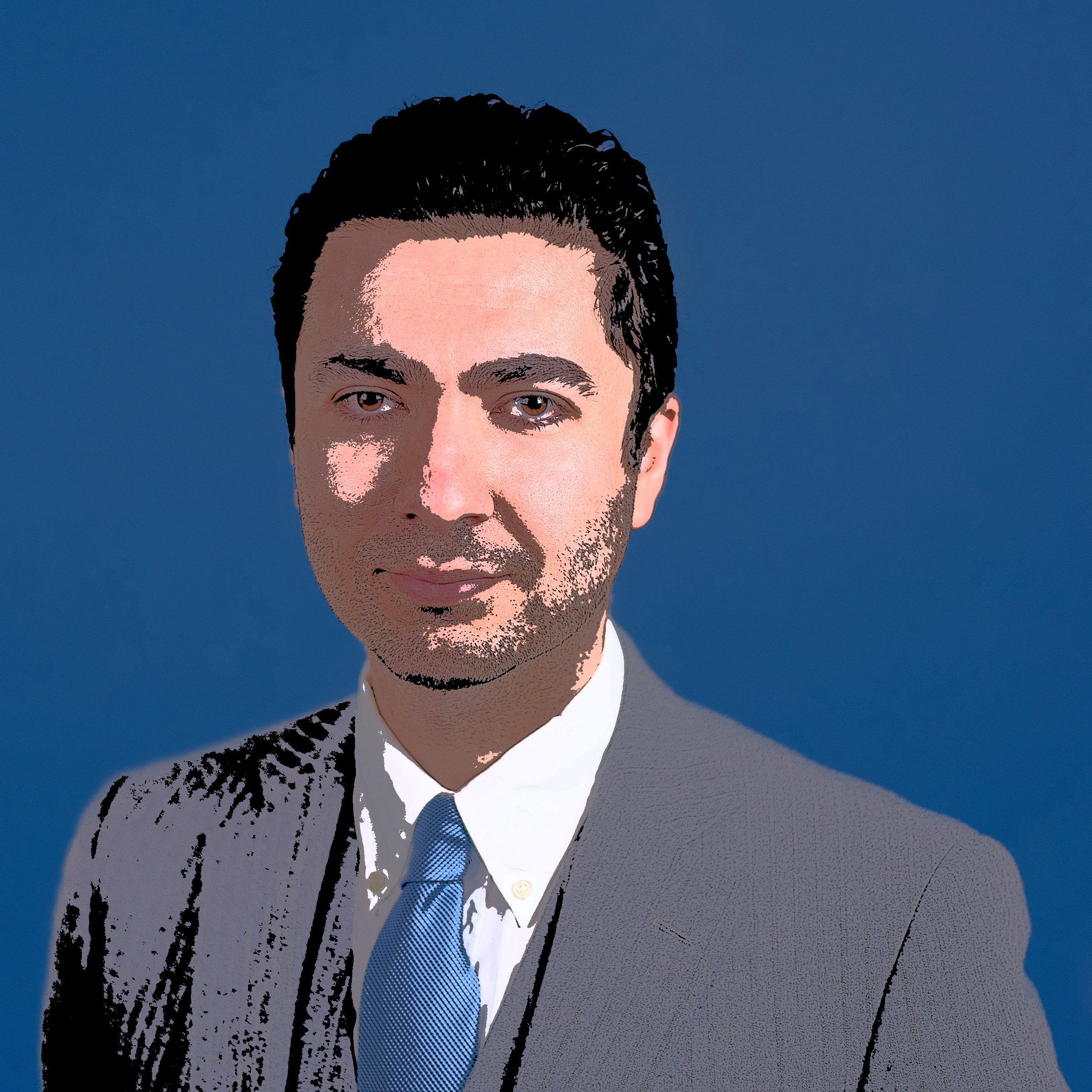 L'image présente un homme en costume, avec une chemise blanche et une cravate bleue. Il a les cheveux noirs et выглядит souriant. Le fond de l'image est bleu, ce qui contraste avec son costume plus sombre. Son expression semble confiante et professionnelle.