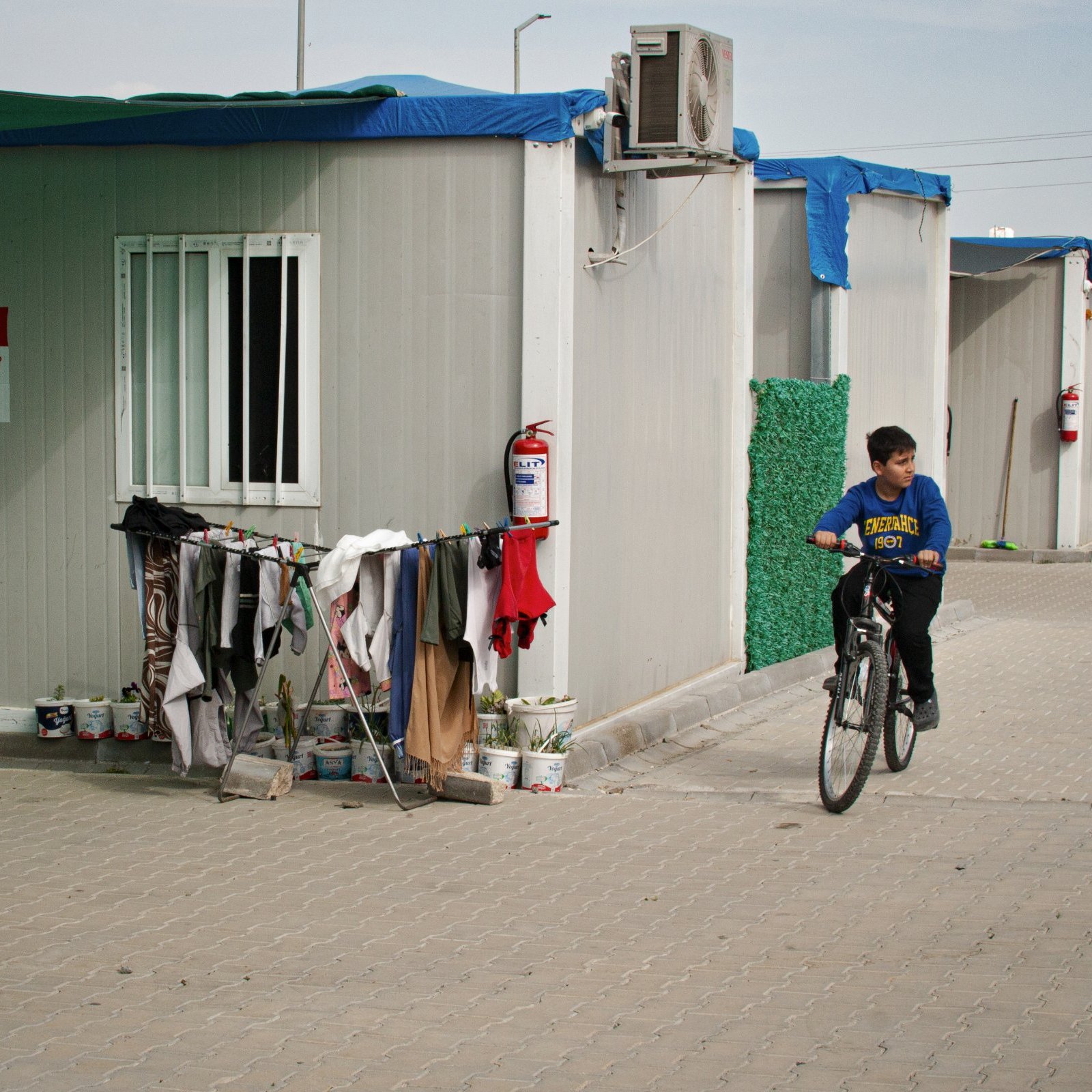 Un enfant à vélo passe près de cabines modulaires et de vêtements accrochés.