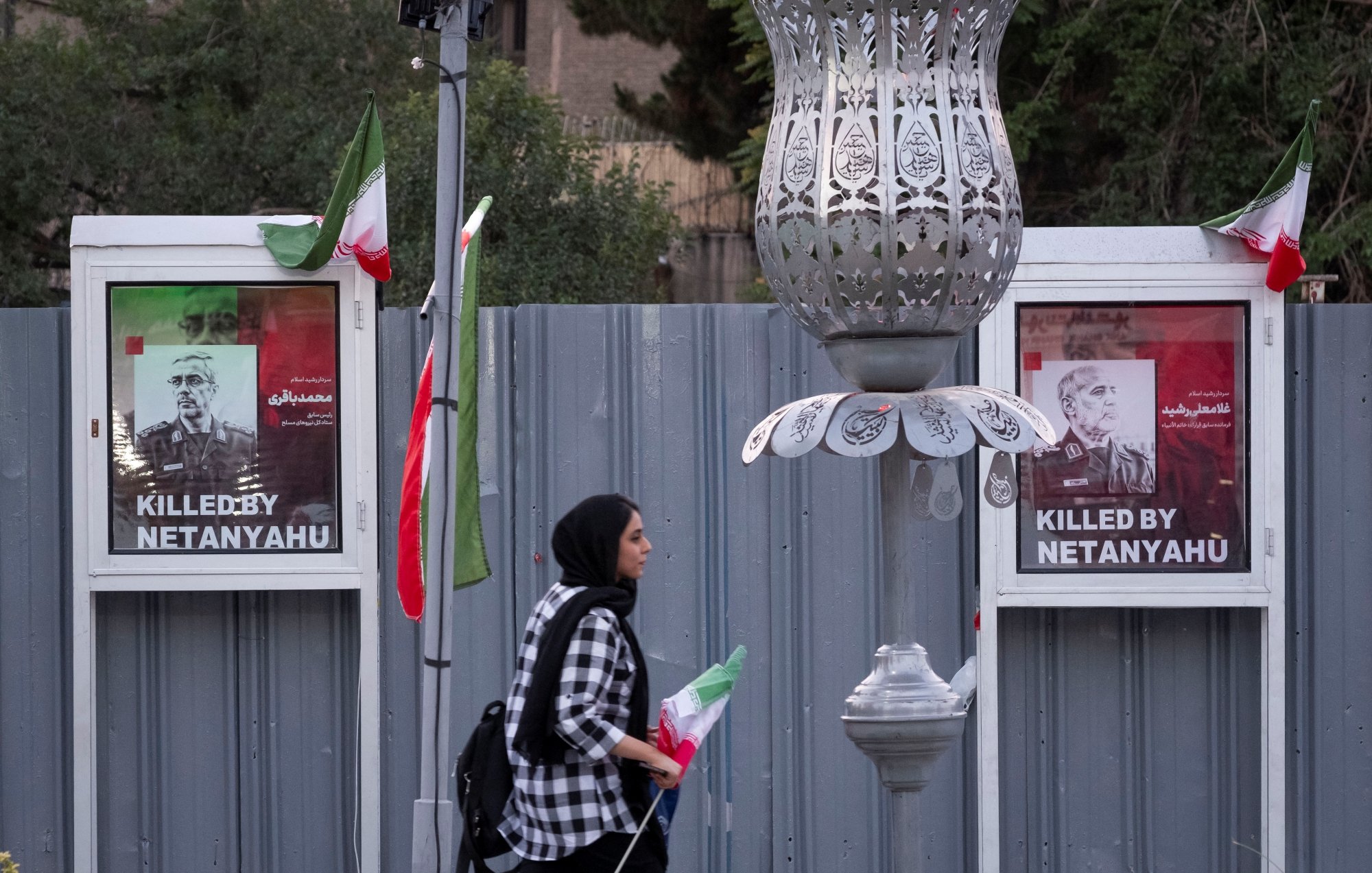 Deux affiches de victimes avec le texte "Killed by Netanyahu", une femme passe avec un drapeau.