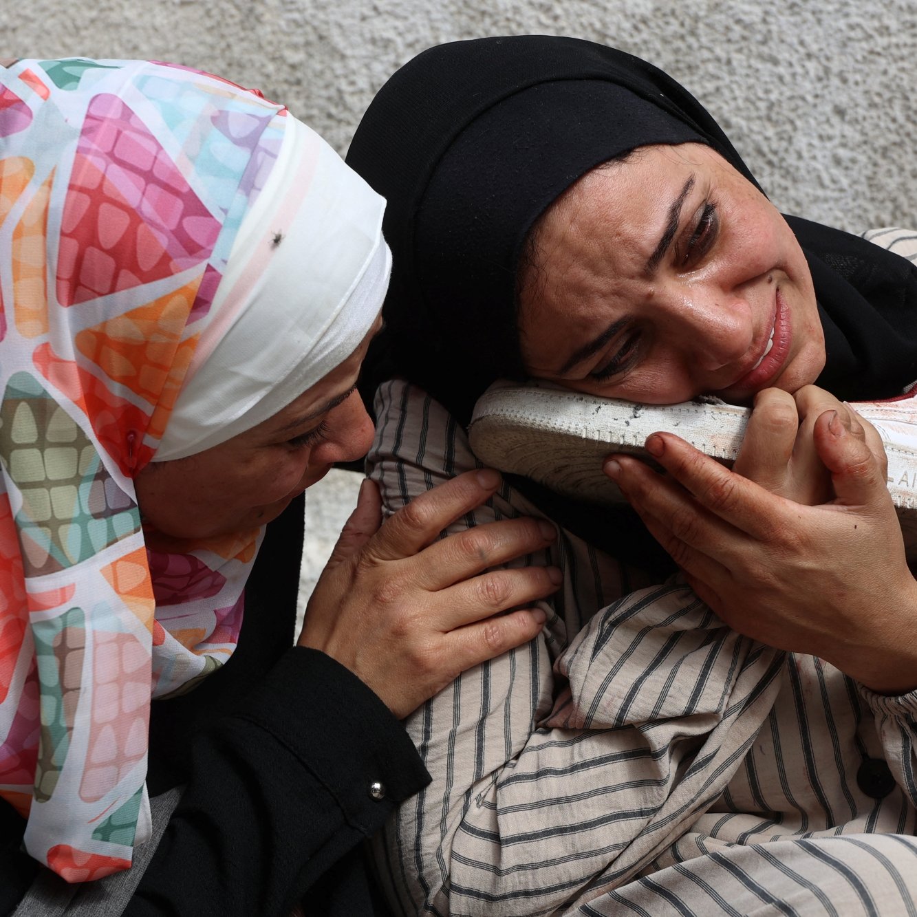 Deux femmes en pleurs, l'une réconfortant l'autre qui tient une chaussure, exprimant une profonde tristesse.