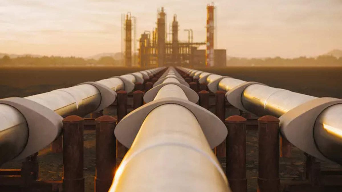 L'image montre une vue d'un long pipeline qui s'étend vers une installation industrielle en arrière-plan. Les tuyaux sont disposés sur des supports et semblent converger vers l'usine, éclairée par une lumière dorée, probablement au lever ou au coucher du soleil. L'environnement autour est vaste et dégagé, avec des montagnes lointaines à l'horizon, créant une ambiance industrielle mais aussi naturelle.