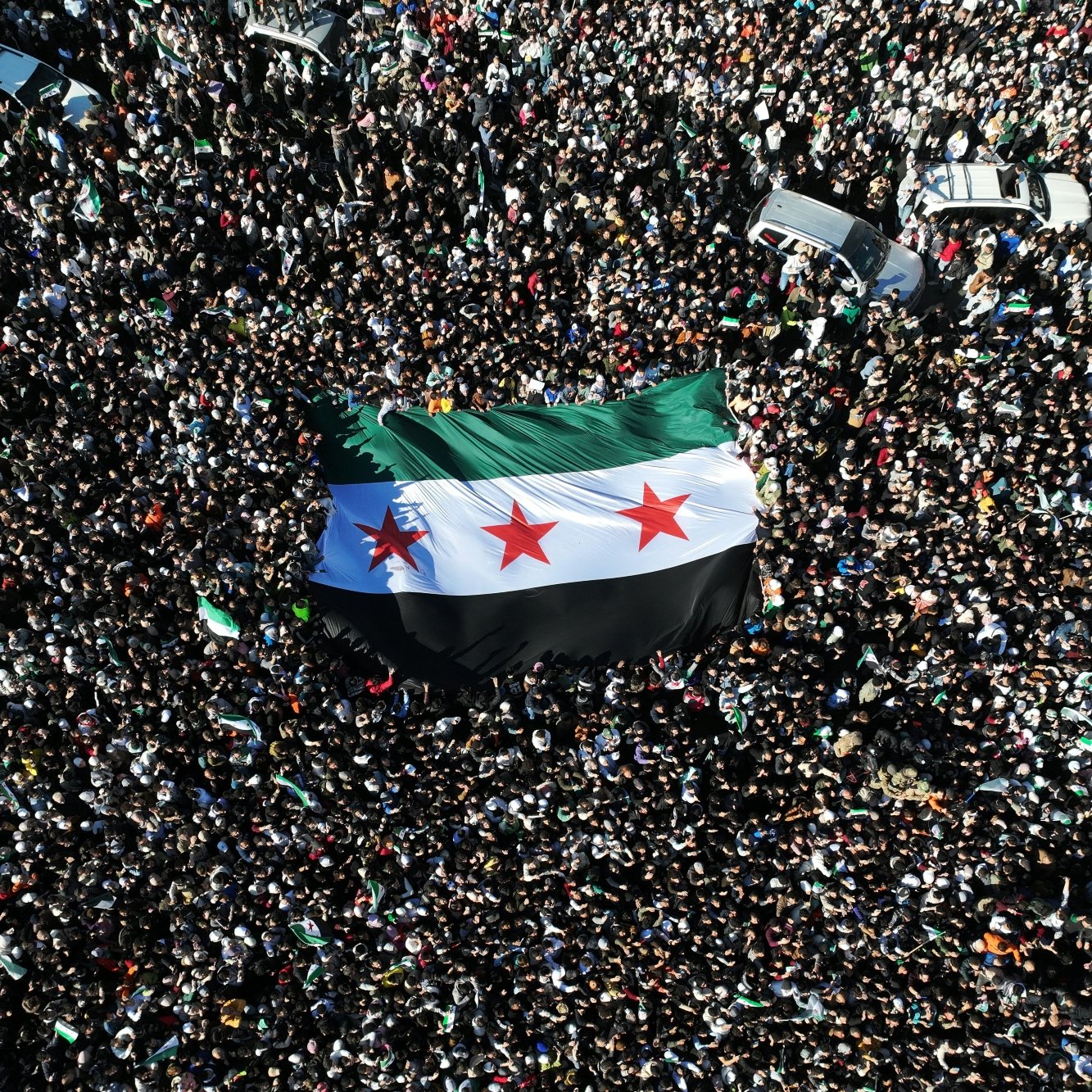 Una grande folla con una bandiera siriana al centro.